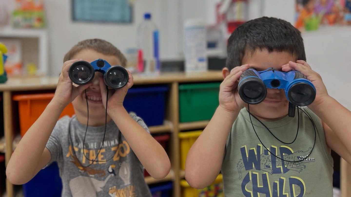 Two boys peering through toy binoculars in their classroom