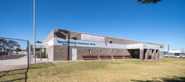 The Yuma site: a long single-story building with a covered entrance and benches along the front, a fenced yard to one side, and open lawn in front, under a clear Arizona sky.